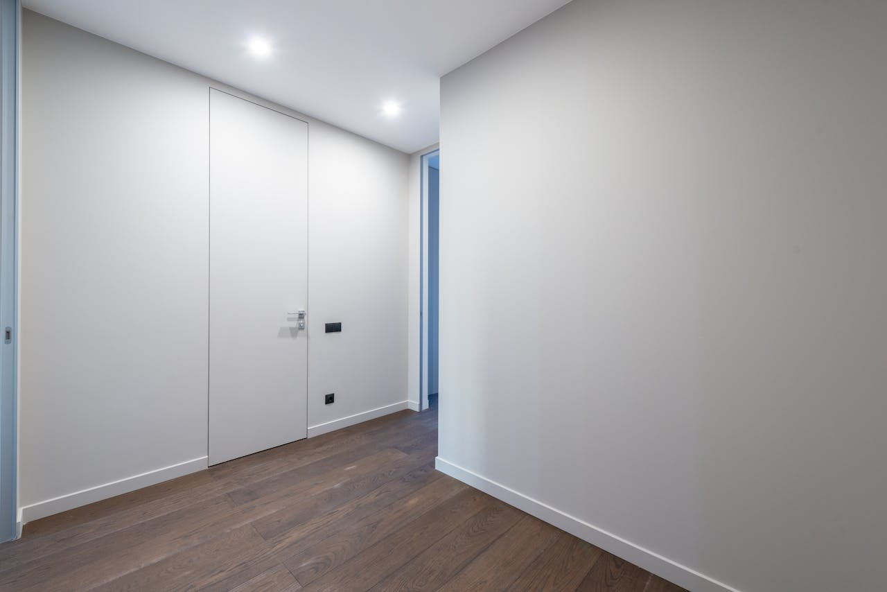 our-services-1 A minimalist indoor corridor featuring sleek doors and wooden flooring under bright lighting.